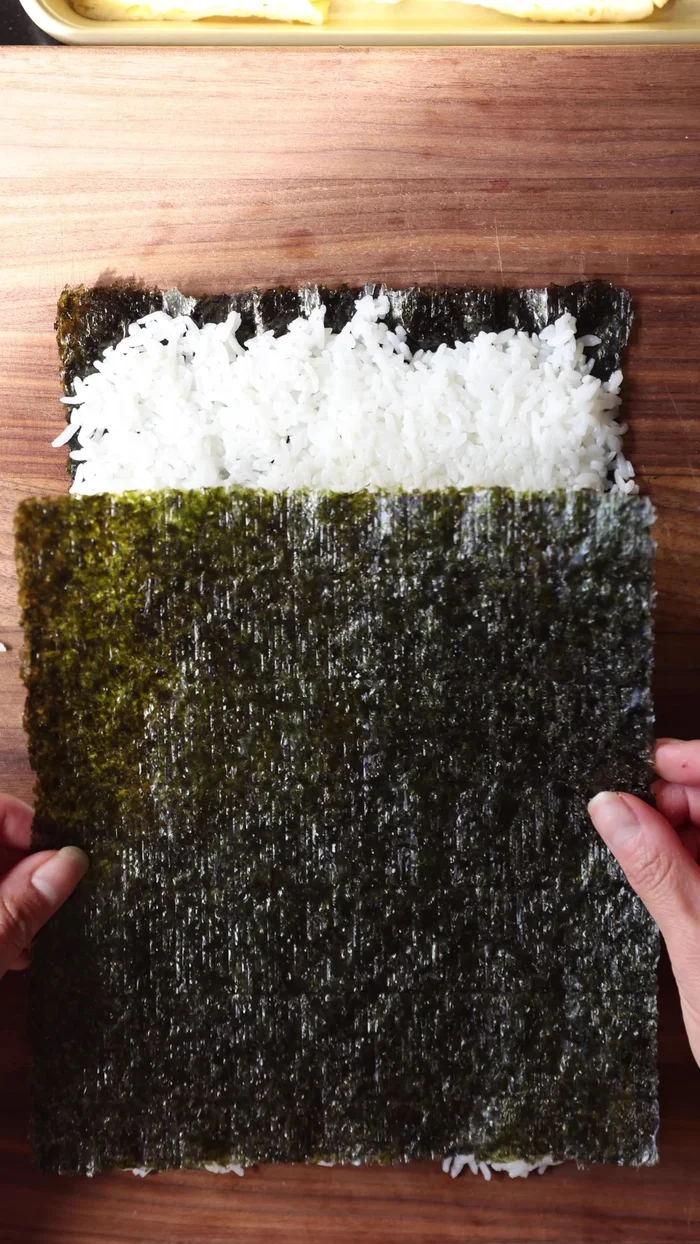 Roll the Spiral Kimbap tightly, drizzle with sesame oil, and cut into 1/2-inch thick pieces.