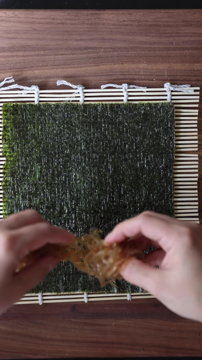 Assemble Chunky Kimbap: Place seaweed sheet (shiny side down) on bamboo mat. Layer fillings: sauteed tanghulu/verelli, Korean omelette, spinach, tanmuji, bulgogi, carrots. Shape rice into a chunky log and place on top. Smear stray rice grains to act as glue.