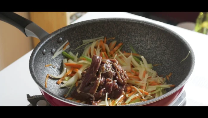 Add the marinated bulgogi beef to the skillet with the vegetables and some sauce.