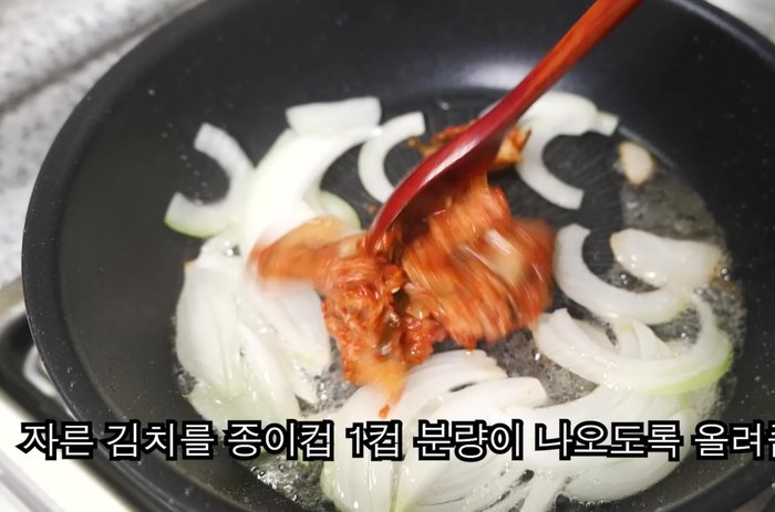 Set aside the fried egg. Roughly chop an onion and add it with kimchi (1 cup), 1/2 spoon gochujang, and 1/2 spoon sugar (omit sugar if using sweet kimchi). Stir-fry evenly in cooking oil.