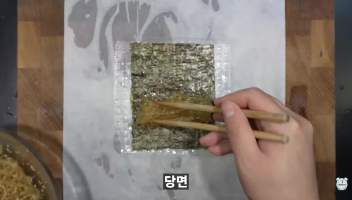 Place a piece of paper towel on a cutting board, place the seaweed and noodles on the soaked paper, and roll them up well. Put cooking oil on a pan, put the seaweed on it, and fry it until golden brown.