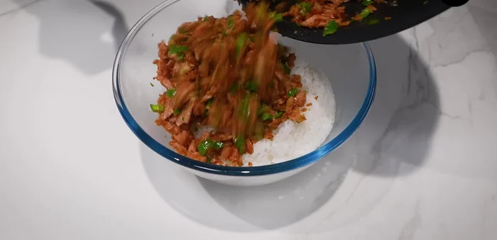 Add the stir-fried chili ham to two bowls of cooked rice. Drizzle with sesame oil and mix gently.
