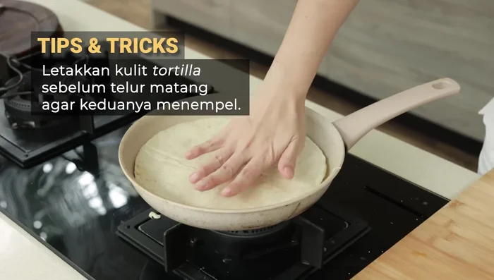 Place a tortilla wrap on top of the egg mixture, lightly butter the top of the tortilla wrap.