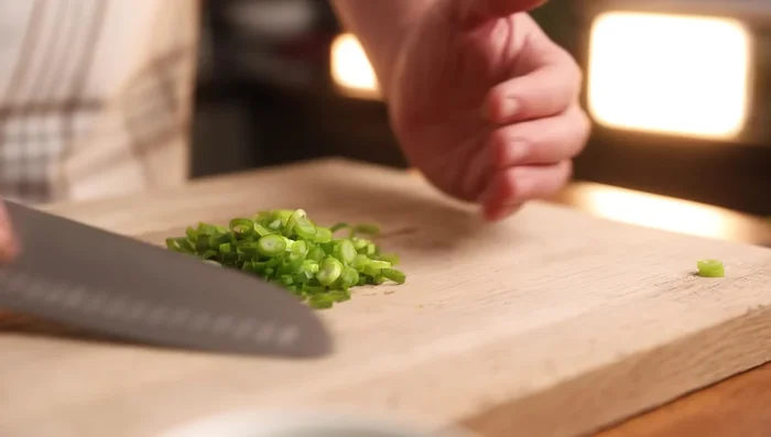 Prepare aromatics: Finely slice spring onion greens, dice half a white onion, and dice chili. Crush garlic and add to the bowl.