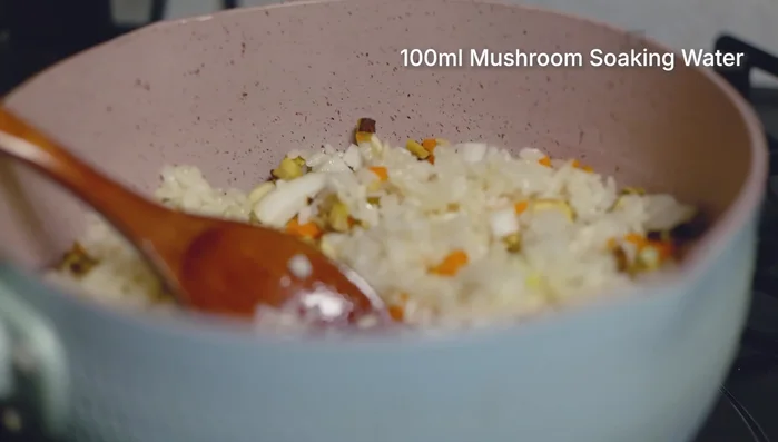 Add the water used to soak the shiitake mushrooms and stir-fry for about 1 minute, ensuring the rice absorbs the mushroom liquid.
