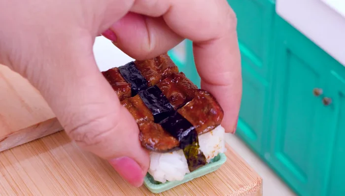 Prepare sushi: Place eel on top of seaweed, add a thin layer of rice, cucumber, crabstick, and salmon. Roll up and place additional eel on top.