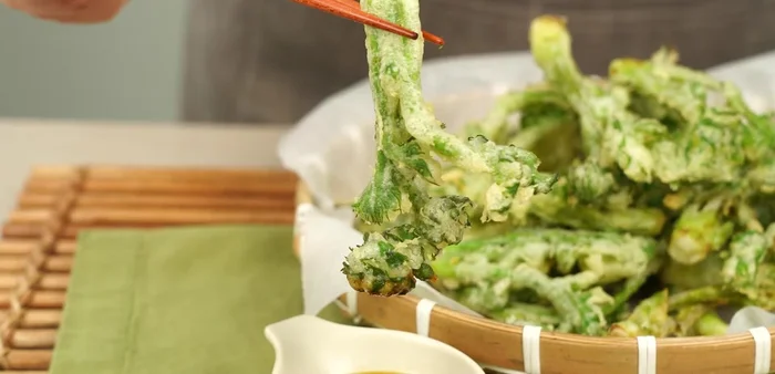 Carefully place the battered fiddleheads into the hot oil. Fry until golden brown and crispy.
