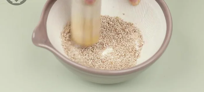 Transfer the mixture into a container, add coarsely ground sesame seeds, and a little sesame oil. Mix lightly.