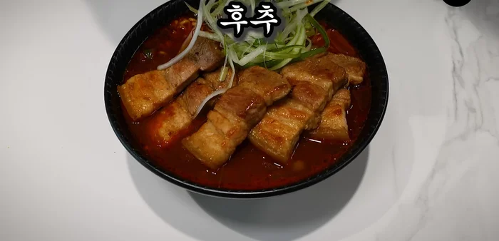 Place cooked noodles in a bowl, top with the pork belly, green onion salad, and plenty of pepper.