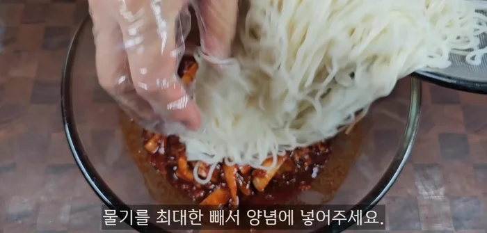 Drain the noodles well and add them to the prepared kimchi seasoning. Add 2 tablespoons of sesame seeds.
