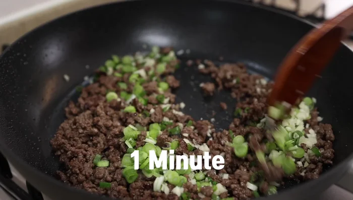 Add the white parts of the green onions and garlic to the beef, stir-fry for 1 minute.