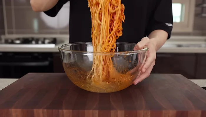 In a bowl, mix noodles with sesame oil and sauce.