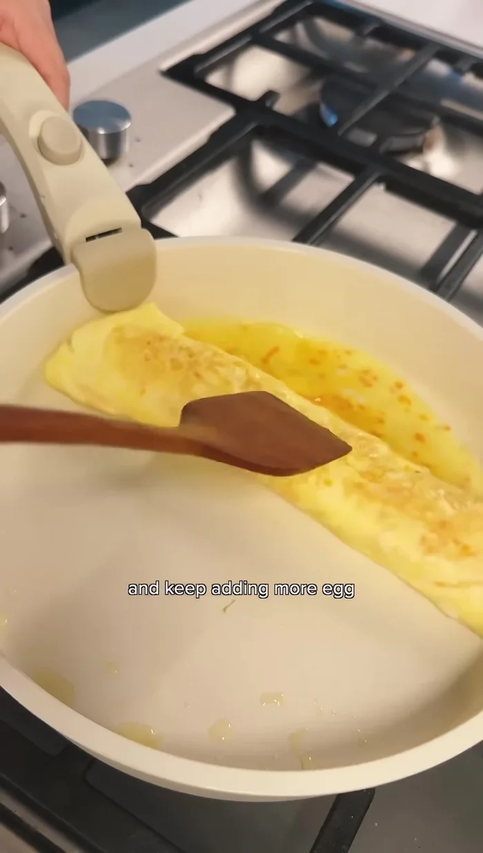Roll the omelette from one end, continuously adding more egg mixture. (Kanari - Rolled Omelette)