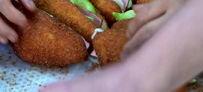 Assemble the Yak Croquette sandwich: Place the fried Yak Croquette in a golden fried bun, layer lettuce, cucumber, ham, and top with the cabbage, carrot, and apple filling. Drizzle with ketchup.